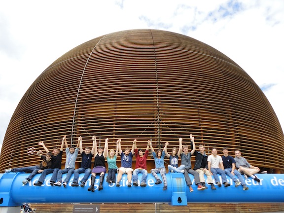 Sixteen or more lab group members sitting on a blue pipe.